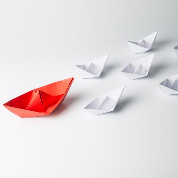 Leadership concept with red paper ship leading among white